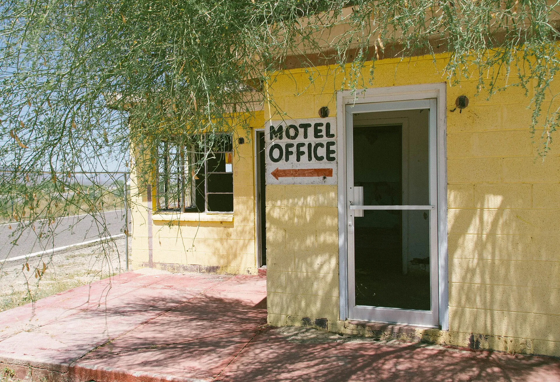 A hand-painted MOTEL OFFICE sign with a red arrow on the yellow cinderblock wall of a small roadside motel